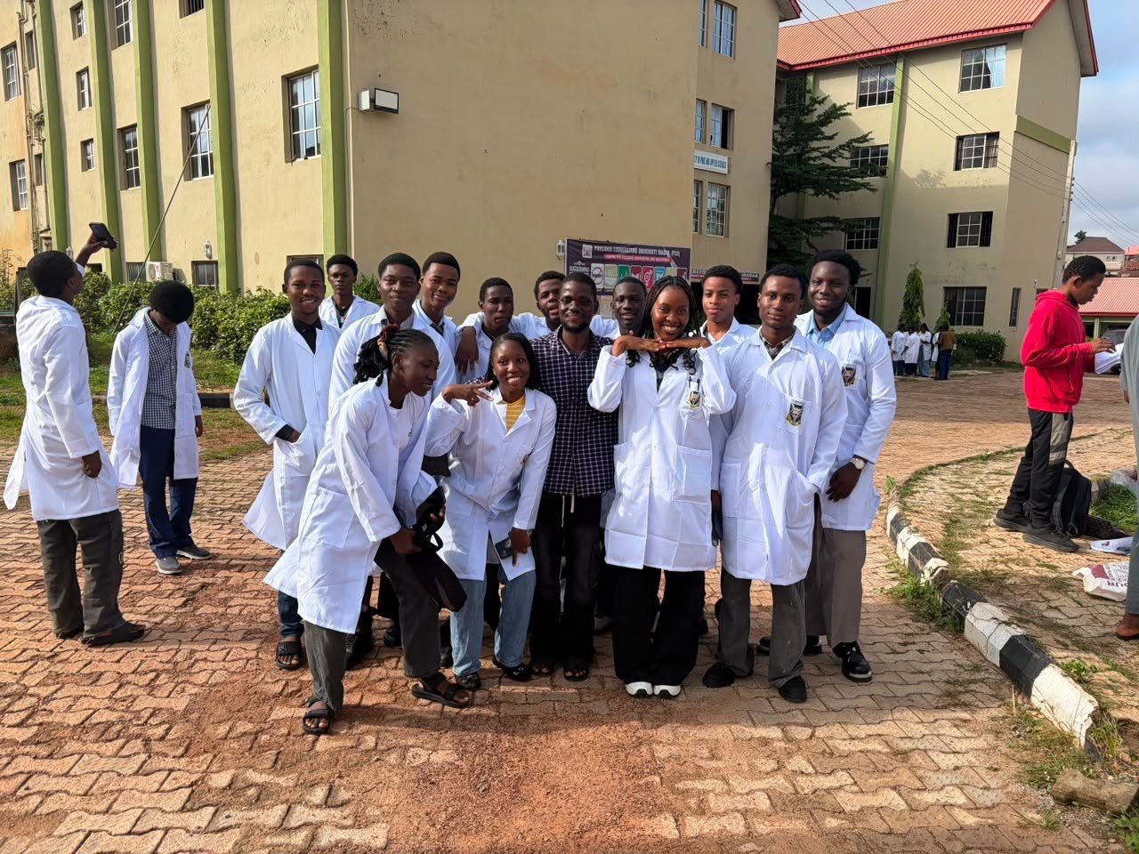 A large group of students in white lab coats outside campus buildings